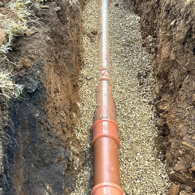 Underground drainage pipe installation in prepared trench.